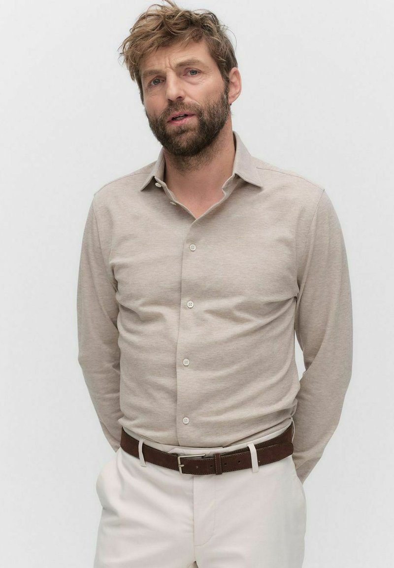 Beige lange mouwen shirt van zachte stof met een klassieke kraag, knoopsluiting aan de voorkant en subtiele textuur, gecombineerd met een witte broek en een leren bruine riem.
