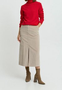 Gonna midi in corduroy beige con uno spacco frontale, abbinata a un maglione rosso e stivali alti al ginocchio marroni con tacco. Il maglione presenta un design con colletto a imbuto.