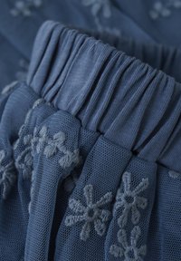 Blått meshtyg med sammanhämtad elastisk midjeband; har broderade blommönster i en ljusare blå nyans. Mjuk textur och lagerdesign.