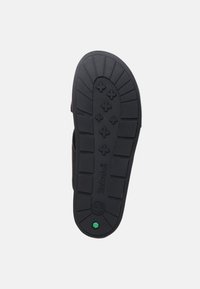 Semelle de sandale en caoutchouc noir avec un motif de texture, présentant un logo central et un accent vert près du talon.