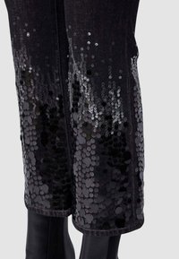 Pantaloni in denim nero con un raffinato ornamento di paillettes lucide nella metà inferiore, creando una transizione graduale da opaco a riflettente.