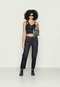 Top cropped preto, jeans escuros de perna reta, botas de tornozelo pretas e uma bolsa crossbody estampada, acessórios com óculos de sol escuros.