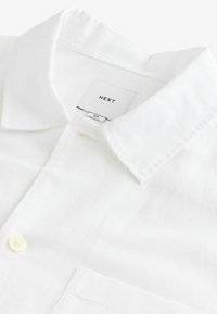 White linen shirt featuring a pointed collar, a single button closure, and a chest pocket. Label reads "NEXT," size M. Soft texture.