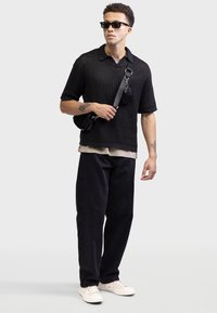 Tricou scurt din tricot negru, pantaloni închiși, adidași albi, gentă crossbody neagră, ochelari de soare; material texturat și croială relaxată.