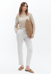 Beige trui met een losse fit, lichte linnen broek en geweven tan muilletjes. Draagt een grote beige tote bag van textuur.