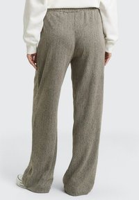 Wijde broekspijpen van een gestructureerde, lichtbruine stof met een subtiel patroon. Heeft een elastische tailleband en recht gesneden pijpen.