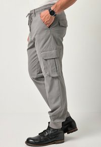 Szare spodnie cargo z elastycznym paskiem, bocznymi kieszeniami i ściągaczami przy kostkach, w zestawie z czarnymi sznurowanymi butami. Wytrzymały materiał o gładkiej fakturze.