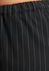 Čierny textil s vertikálnymi bielymi prúžkami, s elastickým pásom a hladkou textúrou, zdôrazňujúci precízny vzhľad.