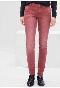 Pantalones ajustados rojos hechos de una tela suave con una textura lisa. Cuentan con un cierre de botón y bolsillos delanteros, combinados con zapatos negros brillantes.