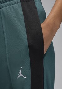 Žali joggeriai su juodu šoniniu vienu, su pilku Jumpman logotipu kairiajame šone ir šonine kišene. Tekstūruotas audinio paviršius.