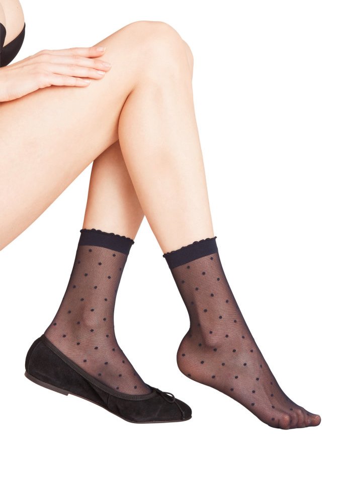 Schwarze Knöchelsocken mit Punkten und gewelltem Bündchen, getragen mit schwarzen Ballerinas. Das durchsichtige Material und die glatte Textur sind sichtbar.
