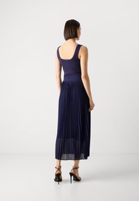 Mornarska midi haljina sa pliseom, koja ima usku, rebrastu bustier i kvadratni izrez na leđima. Ima teksturiranu tkaninu i uparena je sa crnim sandalama.