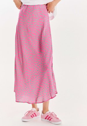 Długa różowa spódnica w zielone kropki, noszona z różowo-białymi butami Adidas, pokazana od talii do stóp.