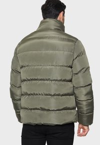 Padded jacket w kolorze oliwkowym, z wysokim kołnierzem, poziomym pikowaniem, błyszczącą fakturą oraz elastycznymi mankietami i dołem.