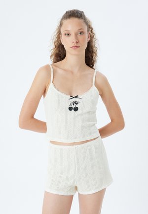 Conjunto de loungewear de algodón beige claro que incluye una parte superior sin mangas con detalles de encaje y un gráfico de cereza, acompañado de pantalones cortos a juego.