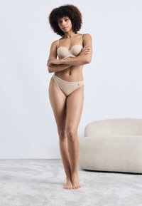 Bež set donjeg rublja koji uključuje grudnjak s podstavom i matching bikini gaćice. Tkanina je glatka s minimalnim šavovima i suptilnim logotipom.