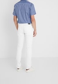 Camisa de manga corta a rayas azul y blanca combinada con pantalones ajustados blancos. Zapatillas blancas complementan el conjunto. La camisa tiene cuello.