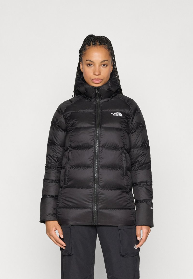 Casaco puffer preto com gola alta e capuz, apresentando um fecho zip, design acolchoado e logótipo no peito e na manga. Textura suave.