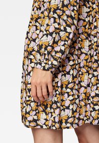 Abito floreale con base nera e motivi gialli, lavanda e bianchi. Maniche lunghe con polsini arricciati e design plissettato.