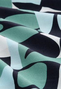 Vzorovaný textil s velkými abstraktními tvary v tónech tyrkysové, světle modré a černé na bílém pozadí. Textura vypadá měkce a hladce.