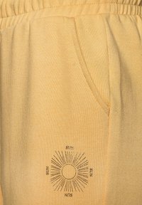 Gelbe Sweatpants verfügen über einen elastischen Bund, Seitentaschen und ein Sonnengrafikmuster mit Strahlen sowie dem in Schwarz gedruckten Wort "SUN".