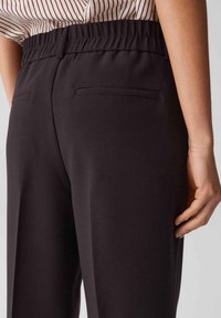 Black trousers with a textured finish, featuring an elastic waistband and two back pockets. Striped shirt visible at the waist.