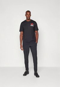 Camiseta deportiva negra con logo rojo de "Adidas Football" en el pecho, combinada con pantalones negros y zapatos negros. Diseño simple y funcional.