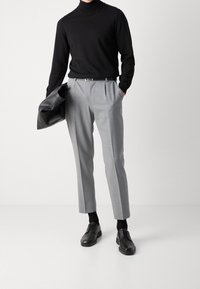 Gray tailored trousers with a relaxed fit, paired with a black turtleneck and black leather shoes, holding a black leather bag.
