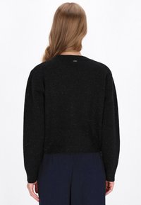 Pulover negru, texturat, cu fulgi metalici, guler rotund și mâneci lungi. Lungime scurtată. Vedere din spate care arată tivul ribbed și designul simplu.