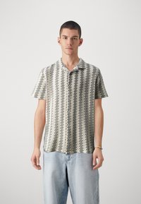 Rövid ujjú ing geometrikus mintával szürke és kr�émszínben, gallérral és gombos záródással. Világoskék, laza szabású farmernadrággal párosítva.