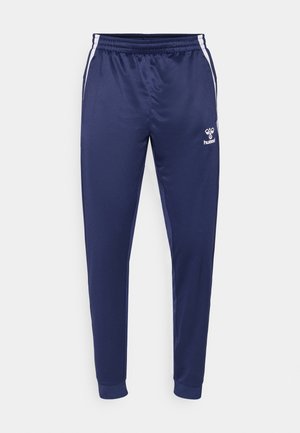 Marineblå sportsbukser lavet af glat stof, med hvide sidelister, elastisk talje og et logo på venstre lår.