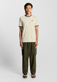Cremfarvet t-shirt med navy krave, prydet med et lille gult logo. Sammen med olivengrønne cargo-bukser og mønstrede sneakers.