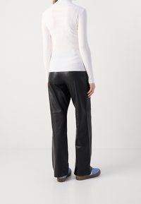 Haut blanc à col roulé côtelé, pantalon large en cuir noir, et baskets bleues avec semelles marron, vus de dos.