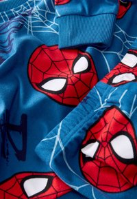 Set di pigiama in pile blu con grandi teste rosse di Spiderman contornate di nero, occhi bianchi e uno sfondo a motivo ragnatela. Texture morbida.