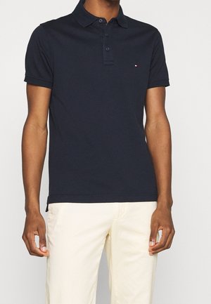 Granatowa koszulka polo z fakturowanej tkaniny, z kołnierzykiem i zapięciem na trzy guziki; posiada małe logo na lewej piersi.