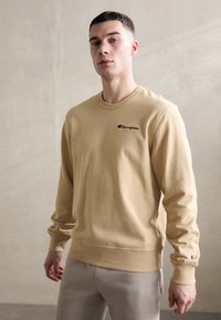 Beige Sweatshirt aus Baumwolle mit Rundhalsausschnitt, langen Ärmeln und einem kleinen gestickten Champion-Logo auf der Brust.