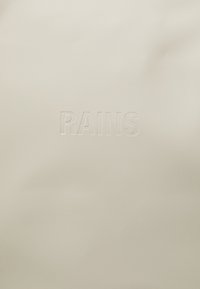 Beige, textúrájú anyag, rajta előnyomott "RAINS" logóval. Simább felület, enyhe fényességgel, minimalista és kortárs dizájn.