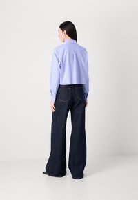 Camicetta cropped viola chiaro con maniche lunghe, polsini con bottone e piega sul retro, abbinata a jeans a gamba larga blu scuro con tasche posteriori.