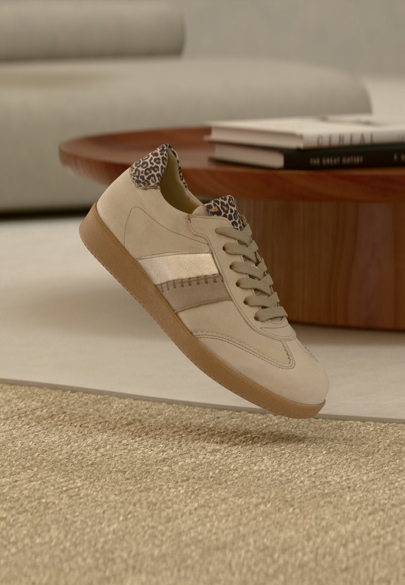 Chaussure de sport beige avec une tige en suède, une bande métallique et des accents imprimés léopard sur le talon. Semelle en caoutchouc avec grip texturé.