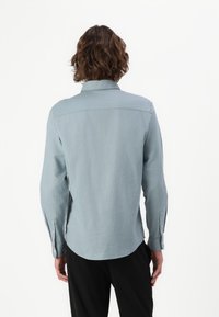 Himmelblaues Langarmhemd mit einer weichen Textur. Verfügt über einen klassischen Kragen und geknöpfte Manschetten. Abgerundeter Saum und Rückensattel-Design.