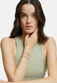 Mehrsträngige Armbänder in verschiedenen Farben, mit Perlen und Edelsteinen, die an einem nackten Handgelenk getragen werden; hellgrüne gerippte Bluse.