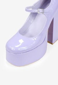 Scarpe Mary Jane a piattaforma in pelle verniciata lavanda con punta arrotondata, cinturino regolabile e tacco largo. Finitura lucida e liscia.
