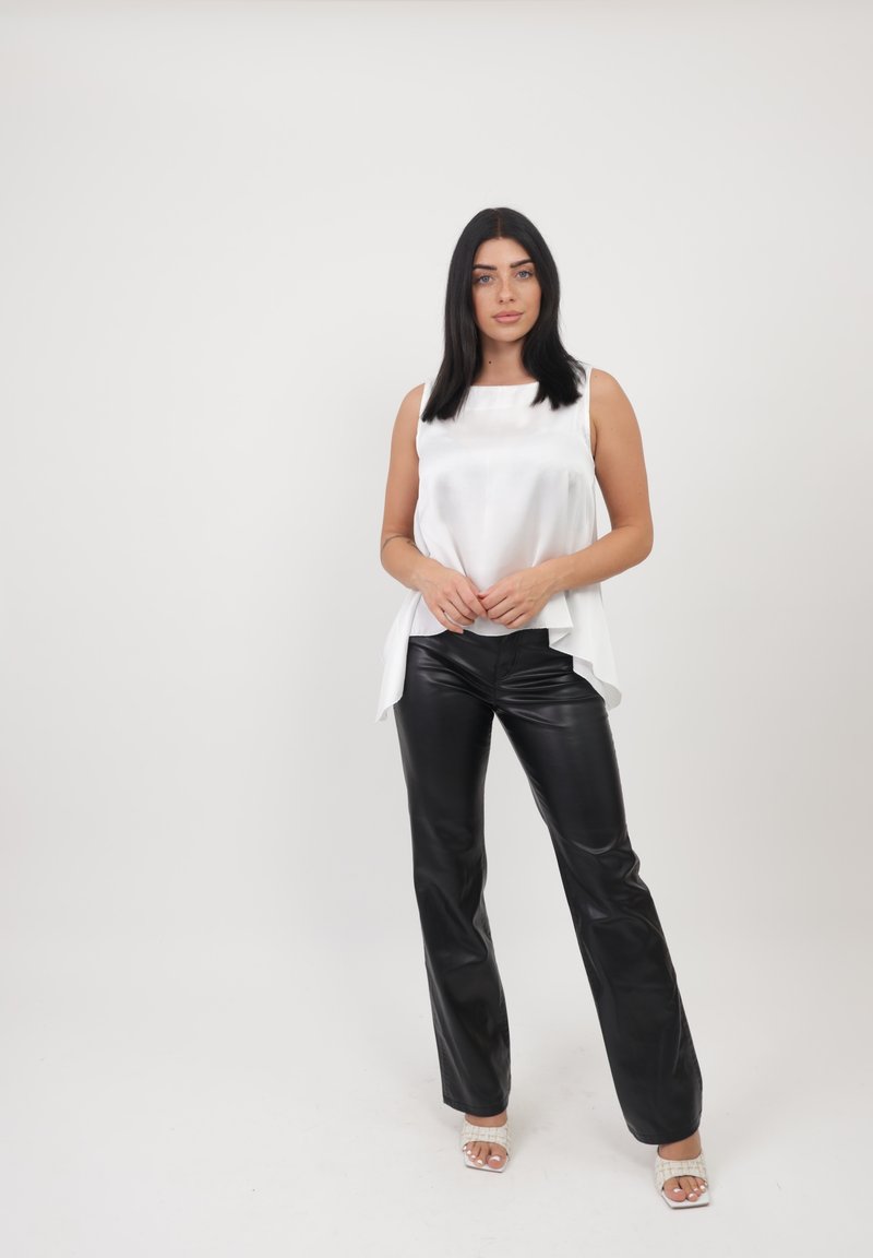 Witte satijnen mouwloze top met een vloeiende uitstraling, gecombineerd met strakke zwarte leren broeken en wit leren sandaaltjes. Eenvoudige, moderne look.