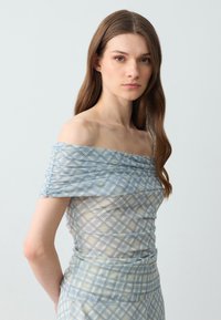 Top leggero a quadri blu chiaro con spalle scoperte, caratterizzato da dettagli arricciati, texture semi-trasparente e design a strati con accenti gialli e beige.