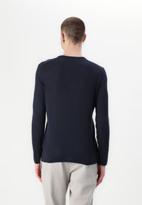 Jūras spēku krāsas garām piedurknēm džemperis ar apaļu kakla izgriezumu, gludu tekstūru un izliekto apakšmalu. Aizmugurē ir sānu uzlīmes akcents.