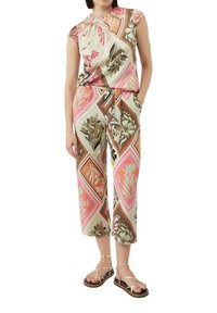 Blumenmuster-Jumpsuit in grünen, rosa und braunen Tönen; hat kurze Ärmel, einen Kordelzug in der Taille und Cropped-Hosen. Getragen mit flachen Sandalen.
