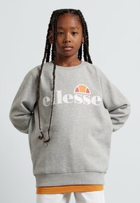 Sudadera gris con cuello redondo, que presenta un logo blanco de "ellesse" y un gráfico naranja encima. Lleva puesta una camiseta naranja, con tejido texturizado.