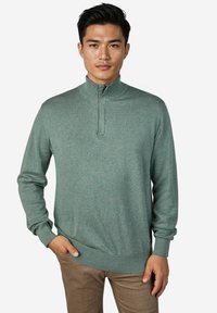 Hellgrüner Strickpullover mit hohem Kragen, halb offenem Reißverschluss, gerippten Bündchen und Saum. Glatte Textur, figurbetontes Design.