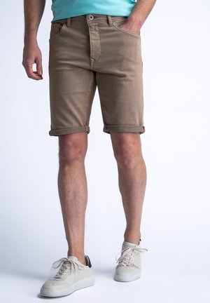 Shorts de mezclilla marrón claro con puños enrollados, diseño de cinco bolsillos y cierre frontal con botón. Se llevan con zapatillas blancas sobre un fondo sencillo.