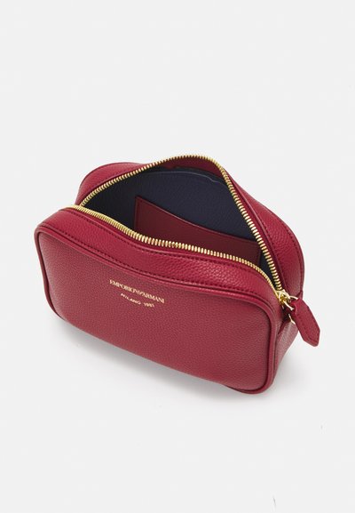 Borsa cosmetica rossa in pelle con finitura testurizzata, cerniera dorata e logo impresso. L'interno presenta una fodera blu e uno scomparto per carte.